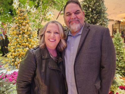 Two adults smiling in front of holiday lights and decorated trees before a youth drug prevention workshop.