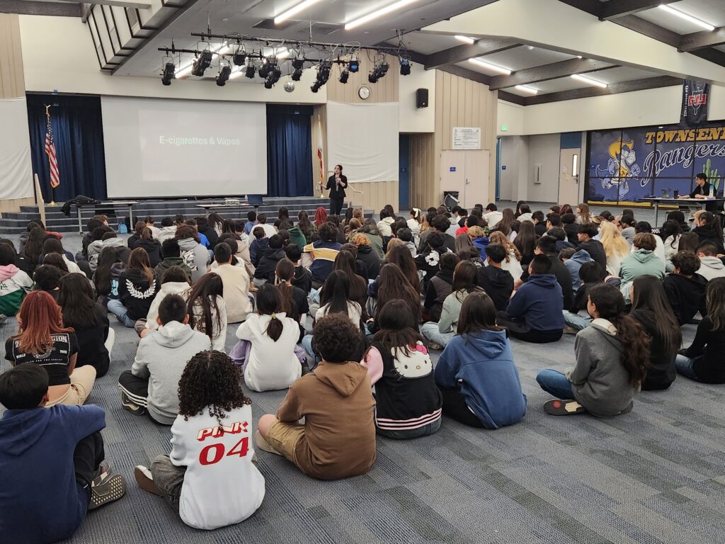 Students attending a youth vaping workshop in a school auditorium during a presentation on e-cigarettes and vapes. Contact Prevention Plus
