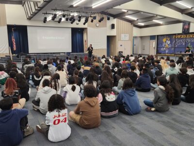 Students attending a youth vaping workshop in a school auditorium during a presentation on e-cigarettes and vapes.