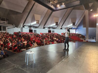 Presenter leading a youth marijuana prevention assembly in a large school auditorium with students seated in rows.