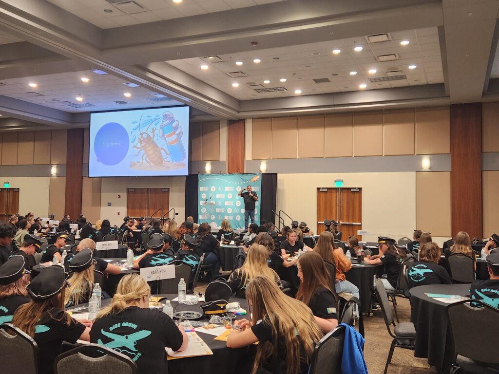 Students attending a marijuana prevention workshop at a youth leadership conference while a presenter speaks onstage.