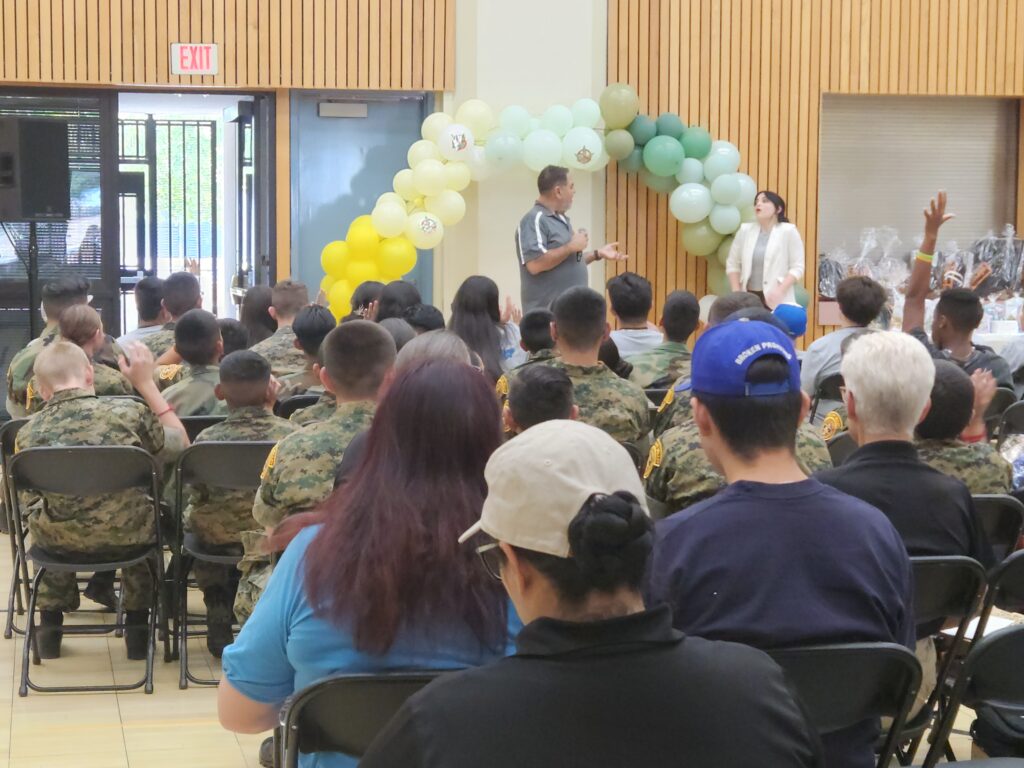 Ray Lozano presenting a youth drug prevention workshop to cadets at Sierra Vista Leadership Academy, with students raising hands during an interactive discussion.