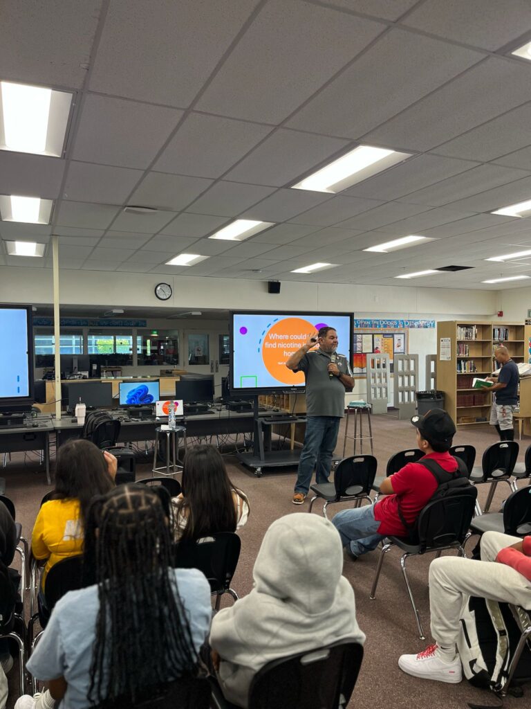 Ray Lozano presenting a youth drug prevention session to students in a school library while discussing how nicotine products are marketed to teens.