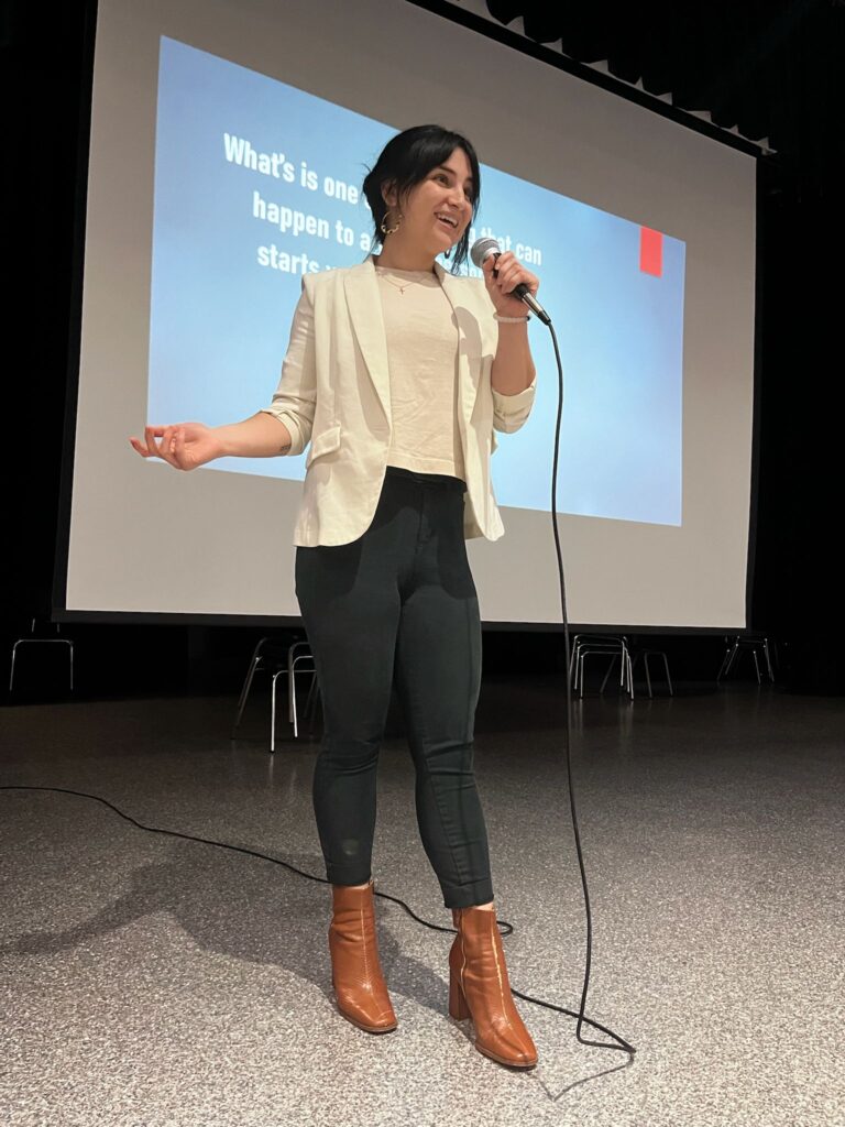 My daughter speaking into a microphone onstage during a youth drug prevention workshop, standing in front of a projected slide.